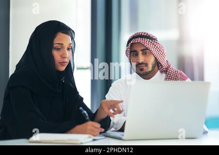 Wenn Arbeit zu erledigen ist, kommen sie dazu. Zwei muslimische Kollegen, die zusammen einen Laptop in einem modernen Büro verwenden. Stockfoto