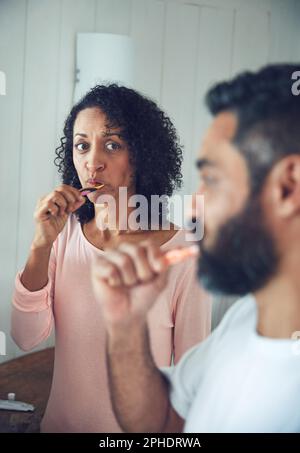 Ich liebe es zu wissen, was er denkt. Eine reife Frau, die ihren Mann ansieht, während sie sich im Bad die Zähne putzt. Stockfoto