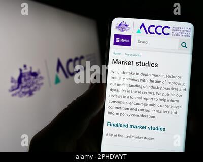 Person, die ein Smartphone mit einer Website der Australian Competition and Consumer Commission auf dem Bildschirm mit Logo hält. Konzentrieren Sie sich auf die Mitte des Telefondisplays. Stockfoto
