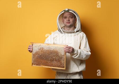 Imker in einheitlichem Bienenstockrahmen mit Wabenstruktur auf gelbem Hintergrund Stockfoto