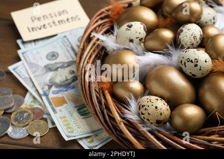 Geld, Karte mit Phrase Pensionsinvestitionen in der Nähe von vielen goldenen und Wachteleiern in einem Nest auf einem Holztisch Stockfoto