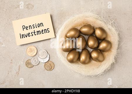 Goldene Eier im Nest, Münzen und Karte mit Phrase Pensionsinvestitionen auf einem leichten Tisch, flach liegend Stockfoto