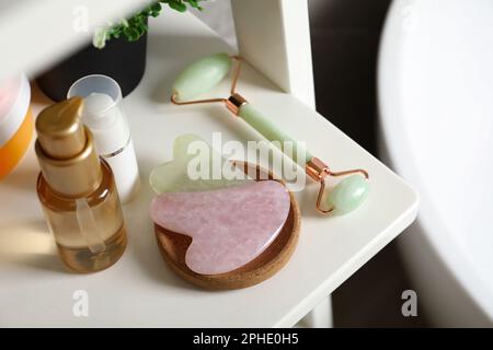 Gua Sha Werkzeuge, Roller mit natürlichem Gesicht und Toilettenartikel auf weißem Regal Stockfoto