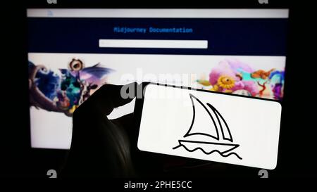 Person, die ein Mobiltelefon mit dem Logo des Unternehmens Midjourney Inc. Für künstliche Intelligenz auf dem Bildschirm vor der Webseite hält. Konzentrieren Sie sich auf das Display des Telefons. Stockfoto