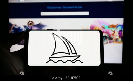 Person, die ein Mobiltelefon mit dem Logo des Unternehmens Midjourney Inc. Für künstliche Intelligenz auf dem Bildschirm vor der Webseite hält. Konzentrieren Sie sich auf das Display des Telefons. Stockfoto