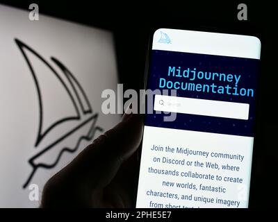 Person, die ein Smartphone mit dem Logo des Unternehmens Midjourney Inc. Für künstliche Intelligenz auf dem Bildschirm vor der Website hält. Konzentrieren Sie sich auf das Display des Telefons. Stockfoto