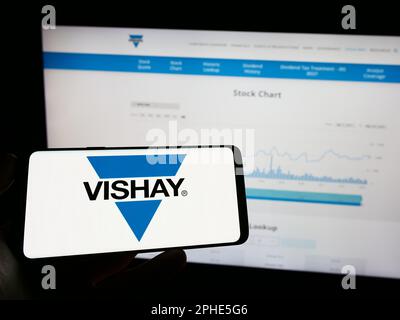 Person, die ein Mobiltelefon mit dem Logo des amerikanischen Unternehmens Vishay Intertech Inc. Auf dem Bildschirm vor der Webseite hält. Konzentrieren Sie sich auf das Display des Telefons. Stockfoto