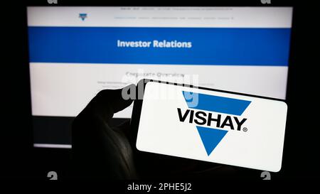 Person, die ein Mobiltelefon mit dem Logo des US-Unternehmens Vishay Intertech Inc. Auf dem Bildschirm vor der Unternehmenswebseite hält. Konzentrieren Sie sich auf das Display des Telefons. Stockfoto