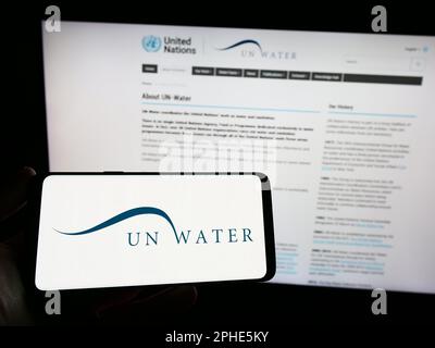 Person, die ein Smartphone mit dem Logo der Organisation UN-Water (UN-Water) auf dem Bildschirm vor der Website hält. Konzentrieren Sie sich auf das Display des Telefons. Stockfoto