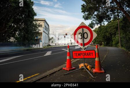 Temporäres Schild mit 30km Geschwindigkeitsbegrenzung und Verkehrskegel am Straßenrand. Autolichtspuren auf der Straße. Auckland. Stockfoto