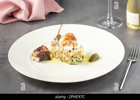 Russischer Salat mit Aioli-Sauce, Garnelen, Tintenfisch und Kapern auf einem weißen Porzellanteller Stockfoto