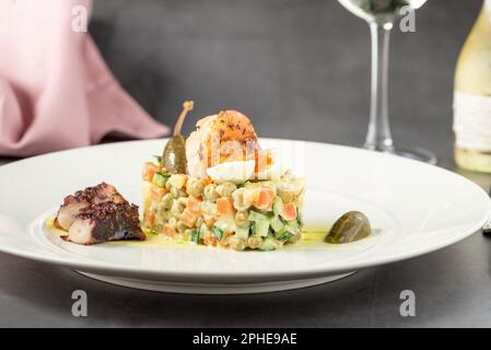 Russischer Salat mit Aioli-Sauce, Garnelen, Tintenfisch und Kapern auf einem weißen Porzellanteller Stockfoto