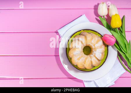 Traditioneller Osterkuchen. Süßes, traditionelles Ostergebäck mit Zuckerpulver, bunten Ostereiern, Frühlingsblumen, rosa gelb Stockfoto