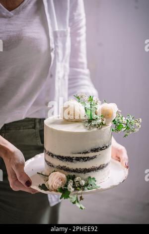 Eine unbekannte Frau, die am Hochzeitstag einen leckeren Kuchen mit Blumen und Zweigen vorführt Stockfoto
