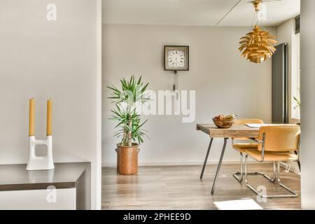 Innendesign des stilvollen, geräumigen Esszimmers mit Holztisch und komfortablen beigen Stühlen in der Nähe einer grünen Topfpflanze Stockfoto