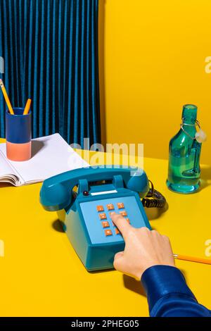 Großer Winkel, in dem eine nicht erkennbare Person Knöpfe auf einem stationären Retro-Telefon in der Nähe einer Flasche Wasser drückt und den Organisator mit einer Tasse Bleistift und einem Stift geöffnet hat Stockfoto