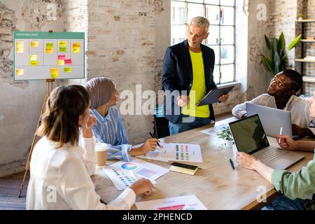 Gruppe von Geschäftsleuten, die arbeiten und Anweisungen von einem erwachsenen Mann entgegennehmen, Portrait von erfolgreicher kreativer Teamarbeit, vielfältig und Stockfoto