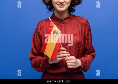 Zugeschnittener Blick auf einen glücklichen Sprachlehrer, der lächelt, während er die Flagge Spaniens isoliert auf blauem Stockbild hält Stockfoto