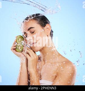 Kiwi, Hautpflege und Wasserspritzer von Frauen, Schönheit und Wellness auf blauem Studiohintergrund. Ruhiges Modell, Dusche und gesunde Früchte für natürliche Vorteile Stockfoto