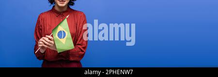 Freigestellte Ansicht eines glücklichen Sprachlehrers, der lächelt, während er die Flagge Brasiliens isoliert auf einem blauen Banner hält Stockfoto