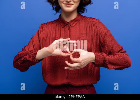 Zugeschnittene Ansicht einer positiven Frau, die eine Geste bedeutet, d. h. einen Dolmetscher auf der Gebärdensprache, isoliert auf blauem, Stockbild Stockfoto
