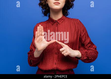 Teilansicht eines Lehrers in burgunderfarbener Bluse mit Gebärdensprache isoliert auf blauem Stockbild Stockfoto