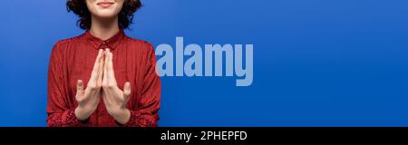 Abgeschnittene Ansicht einer lächelnden Frau, die eine Geste zeigt, die bedeutet, glücklich auf der Zeichensprache isoliert auf blau, Banner, Stock-Bild Stockfoto