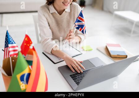 Zugeschnittene Ansicht eines lächelnden Sprachlehrers mit der Flagge von Großbritannien, der während des Online-Unterrichts zu Hause ein Laptop benutzt, Stock Image Stockfoto