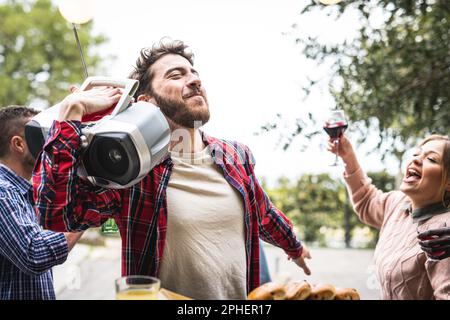 Ein junger bärtiger Mann, der Musik aus einer Boombox von '90 hört, eine Gruppe von Freunden und Familie im Garten Stockfoto