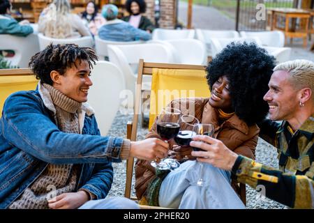 Drei Freunde sitzen auf Liegestühlen und toasten zusammen mit einem Glas Rotwein Stockfoto
