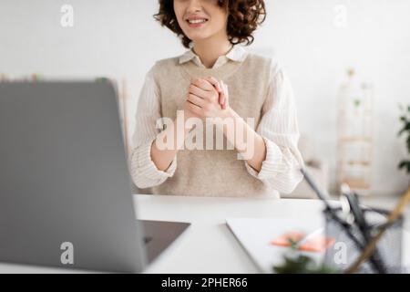Zugeschnittene Ansicht einer lächelnden Frau, die während eines Videochats auf einem verschwommenen Laptop zu Hause in Zeichensprache spricht, Stockbild Stockfoto