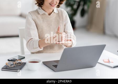 Zugeschnittene Ansicht eines fröhlichen Lehrers, der während des Online-Unterrichts zu Hause ein Hilfewort zur Gebärdensprache zeigt, Stockbild Stockfoto