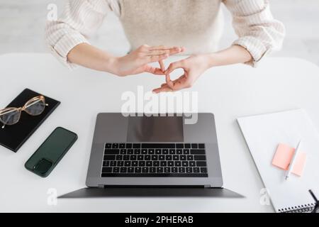 Zugeschnittene Ansicht des Lehrers mit Dolmetschschild auf Körpersprache in der Nähe von Laptop und Smartphone auf dem Schreibtisch, Stockbild Stockfoto