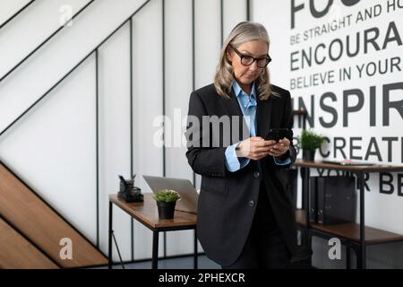 Porträt einer erwachsenen Freiberuflerin mit grauen Haaren, die ein Telefon im Haus hält Stockfoto