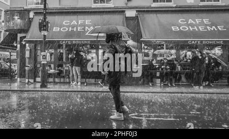 Schwarzweiß-Bild eines Fußgängers, der im schweren Regen in Londons Soho gefangen war. Stockfoto