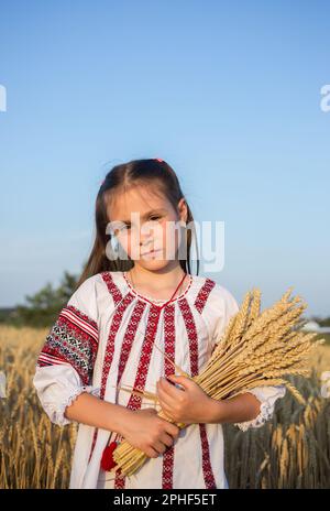 7-jähriges Mädchen in einer bestickten Bluse mit einem Strauß Weizen am Himmel. Ich bin stolz darauf, eine ukrainische, nationale Identität zu sein. Stockfoto