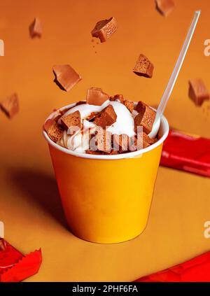 Eine vertikale Nahaufnahme einer hellgelben Tasse gefüllt mit Eis und Schokoladenstücken, die nach unten fallen Stockfoto