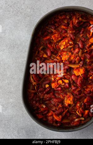 Gesundes Frühstück und Mittagessen, gedünstete rote Bohnen mit Karotten, Zwiebeln und Tomaten, Blick von oben auf eine ovale Keramikrösterei mit gedünsteten Hülsenfrüchten Stockfoto