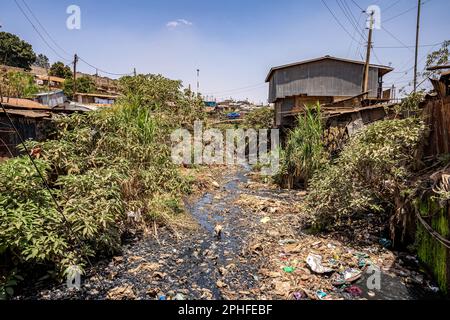 Blick auf einen verschmutzten Fluss, der durch Kibera Slum, Nairobi, Kenia fließt. Kibera ist der größte Slum Afrikas und einer der größten der Welt. Dort leben schätzungsweise 1 Millionen Menschen, die in extremer Armut leben. Eine große Mehrheit der Menschen hat keinen Zugang zu Grundversorgung und medizinischer Versorgung: Nur etwa 20 % der Kibera verfügen über Elektrizität, und das Wasser, das seine Hütten erreicht, ist nicht sauber und verursacht Typhus und Cholera. In den meisten Kibera gibt es keine Toiletten. Die Arbeitslosenquoten sind hoch, und die meisten Menschen können sich keine Bildung für ihre Kinder leisten. Stockfoto