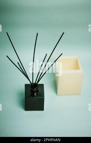 Aroma-Diffusor in einem schwarzen Glasgefäß mit schwarzen Bambusstäbchen auf einem hellblauen vertikalen Hintergrund. Ein Duft für Zuhause. Eine weiße, natürliche Kerze. Dekor, Stockfoto