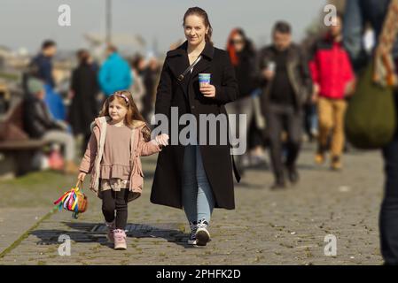 Die junge Mutter und ihre kleine Tochter gehen auf der Moldau unter den anderen Besuchern des Bauernmarktes in Prag spazieren. Stockfoto