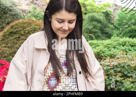 Eine wunderschöne spanische Frau und eine neue Mutter, die in Edinburgh in der Natur spazieren geht, lächelt und nach unten schaut. Brünett und lange Haare. Stockfoto