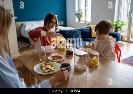 Mutter und zwei Kinder sitzen zu Hause am Küchentisch und essen gemeinsam gesundes Essen am Morgen Stockfoto