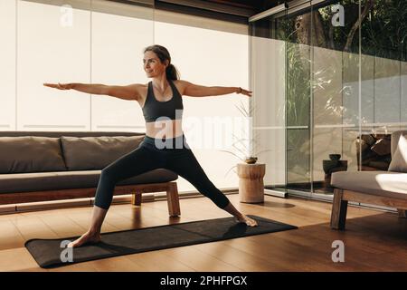 Reife Frau, die während einer Yoga-Sitzung die Krieger-Pose macht. Seniorin, die eine Gleichgewichtsübung auf einer Trainingsmatte macht. Aktive Frau, die eine Heilung praktiziert Stockfoto