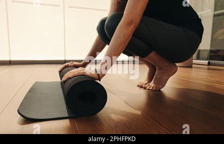 Eine unbekannte Seniorin, die nach einer Yoga-Session eine Matte hochrollt. Ältere Frau nach einer gesunden Fitness-Routine zu Hause. Reife Frau t Stockfoto