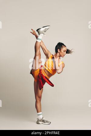 Fit Frau führt ein anspruchsvolles einbeiniges Gymnastiktraining in einem Studio durch und zeigt ihre Flexibilität und Balance. Sportlerin mit schlankem Körper Stockfoto