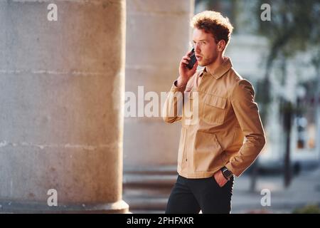 Telefonisch. Eleganter junger Mann in formeller, eleganter Kleidung im Freien in der Stadt Stockfoto