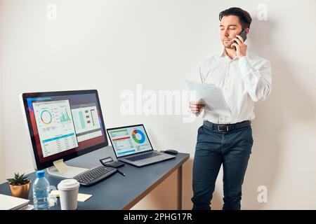 Mann Unternehmer mit Geschäftsgespräch auf dem Handy. Geschäftsmann mit Dokumenten und Smartphone, das mit Daten auf Diagrammen und Grafiken arbeitet Stockfoto