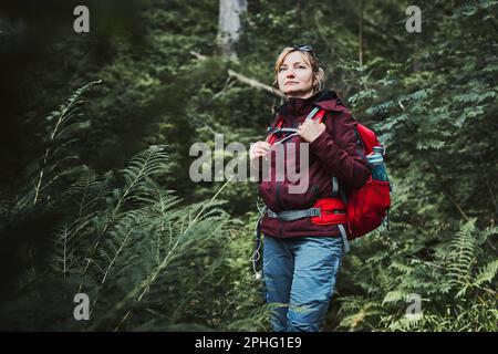 Frau mit Rucksack Wandern im Wald, aktiv verbringen Sommerurlaub in der Nähe der Natur. Frau, die auf einem Pfad zwischen Bäumen läuft Stockfoto