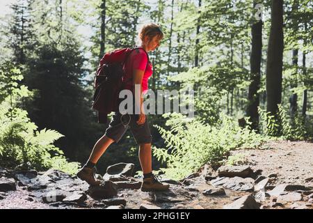 Frau mit Rucksack Wandern in den Bergen, verbringen Sommerurlaub in der Nähe der Natur. Frau, die auf dem Weg zwischen Büschen und Bäumen geht Stockfoto